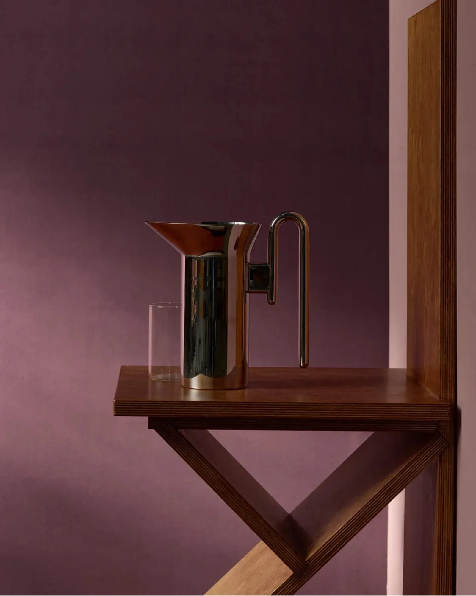 Modern chrome pitcher and glass on wooden shelf against a purple wall in luxury interior