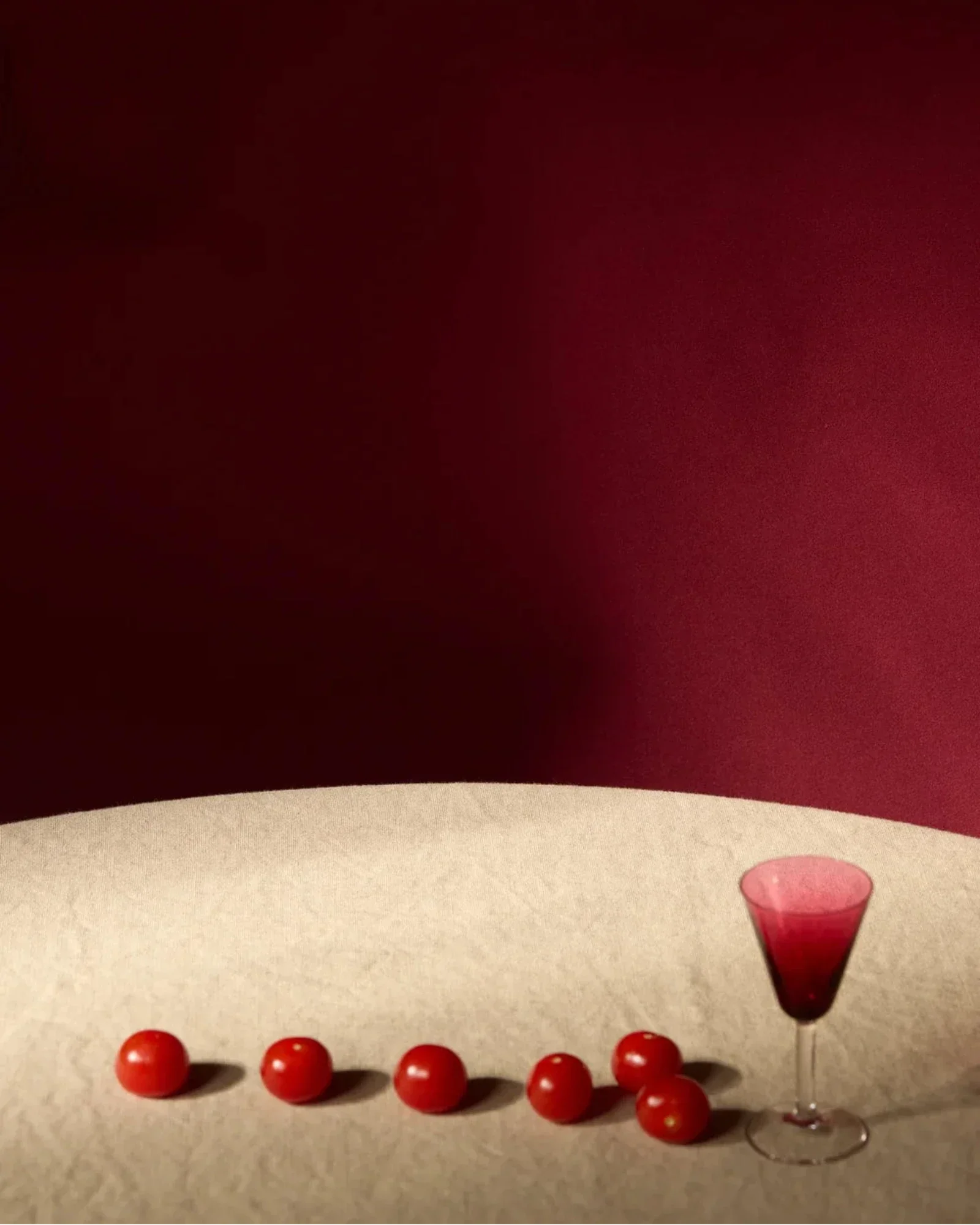 Elegant wine glass and red cherry tomatoes on a light table with a deep red background