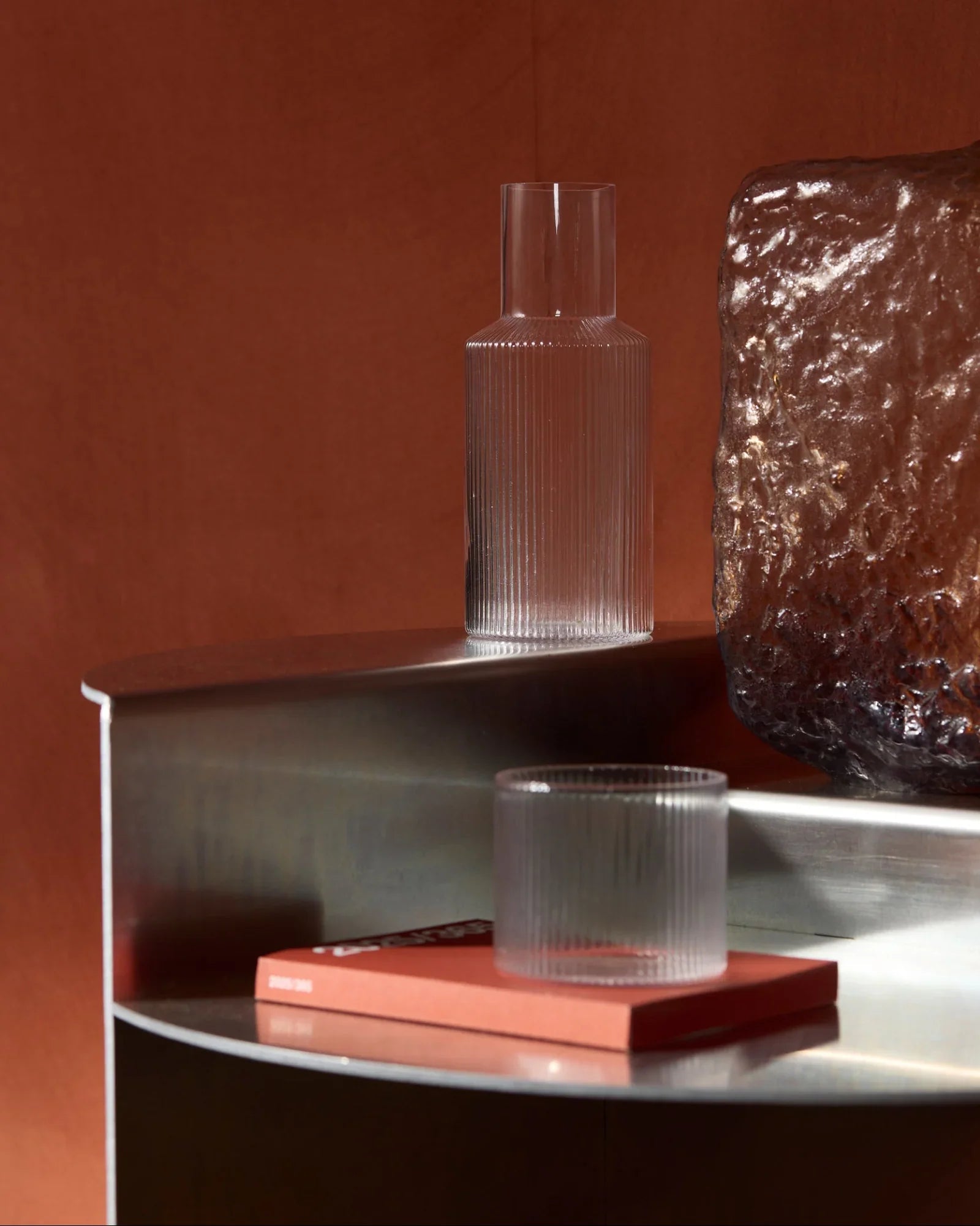 Modern ribbed glass carafe and tumbler on a metal shelf with a textured glass sculpture