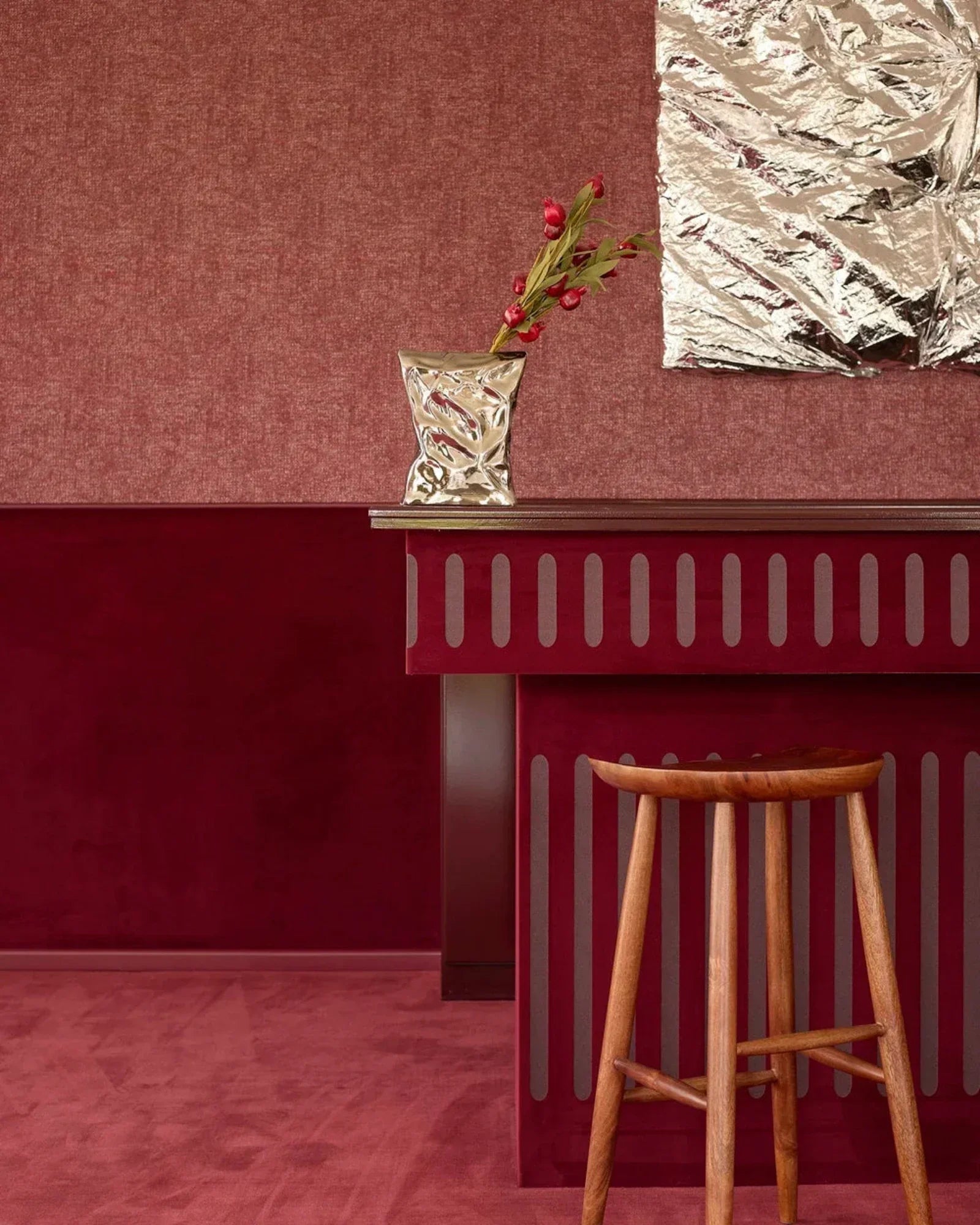 Modern luxury interior with wooden stool, red accent wall, metallic vase and abstract art