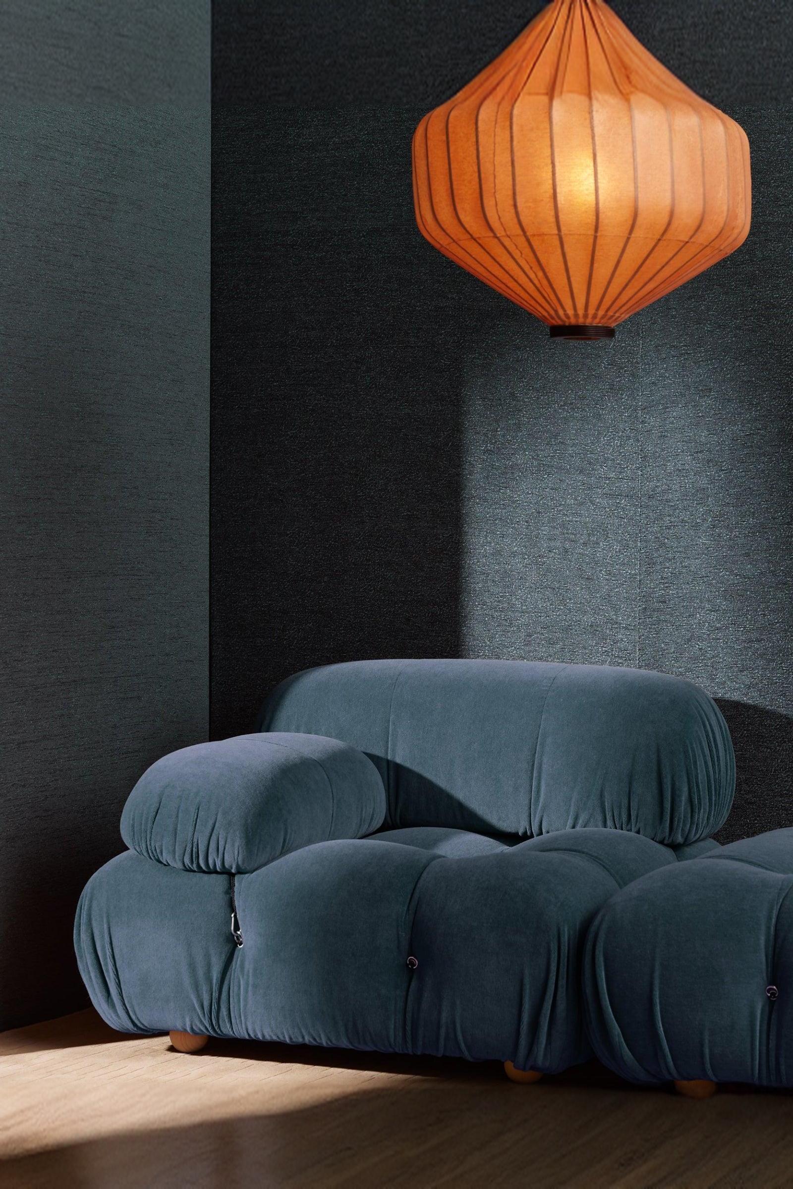 Modern cobalt blue velvet armchair with padded design and an orange pendant lamp in a luxury interior