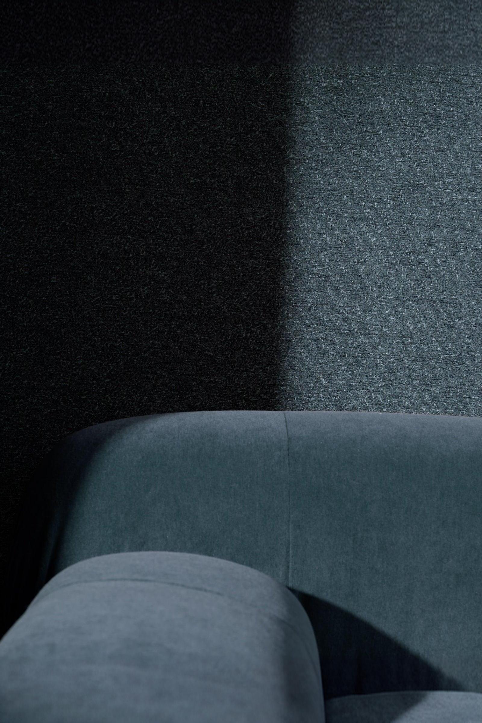 Minimalist luxury interior with curved blue velvet sofa against dark textured wall