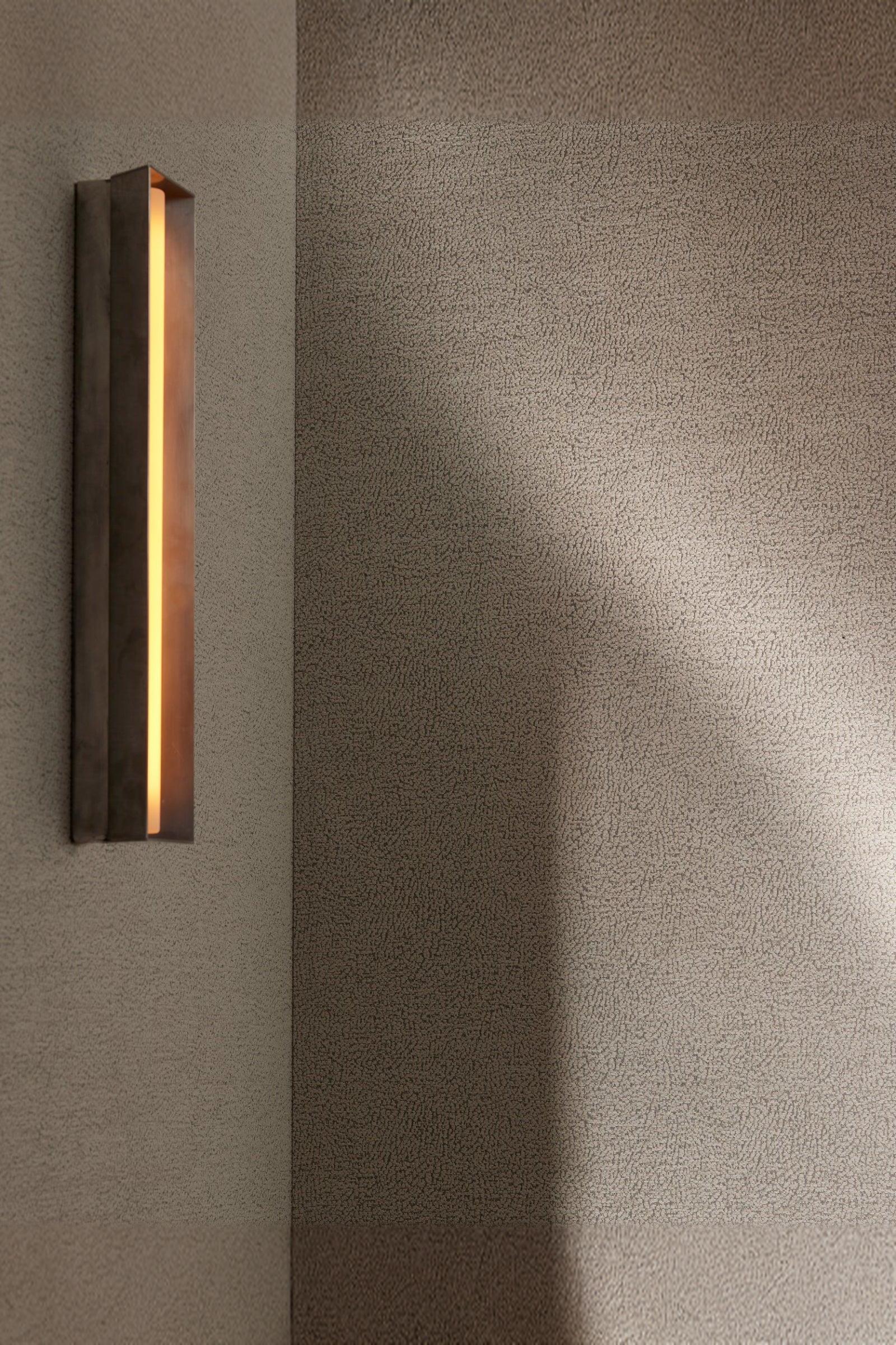 Modern wall sconce with warm light on textured neutral wall in luxury interior setting