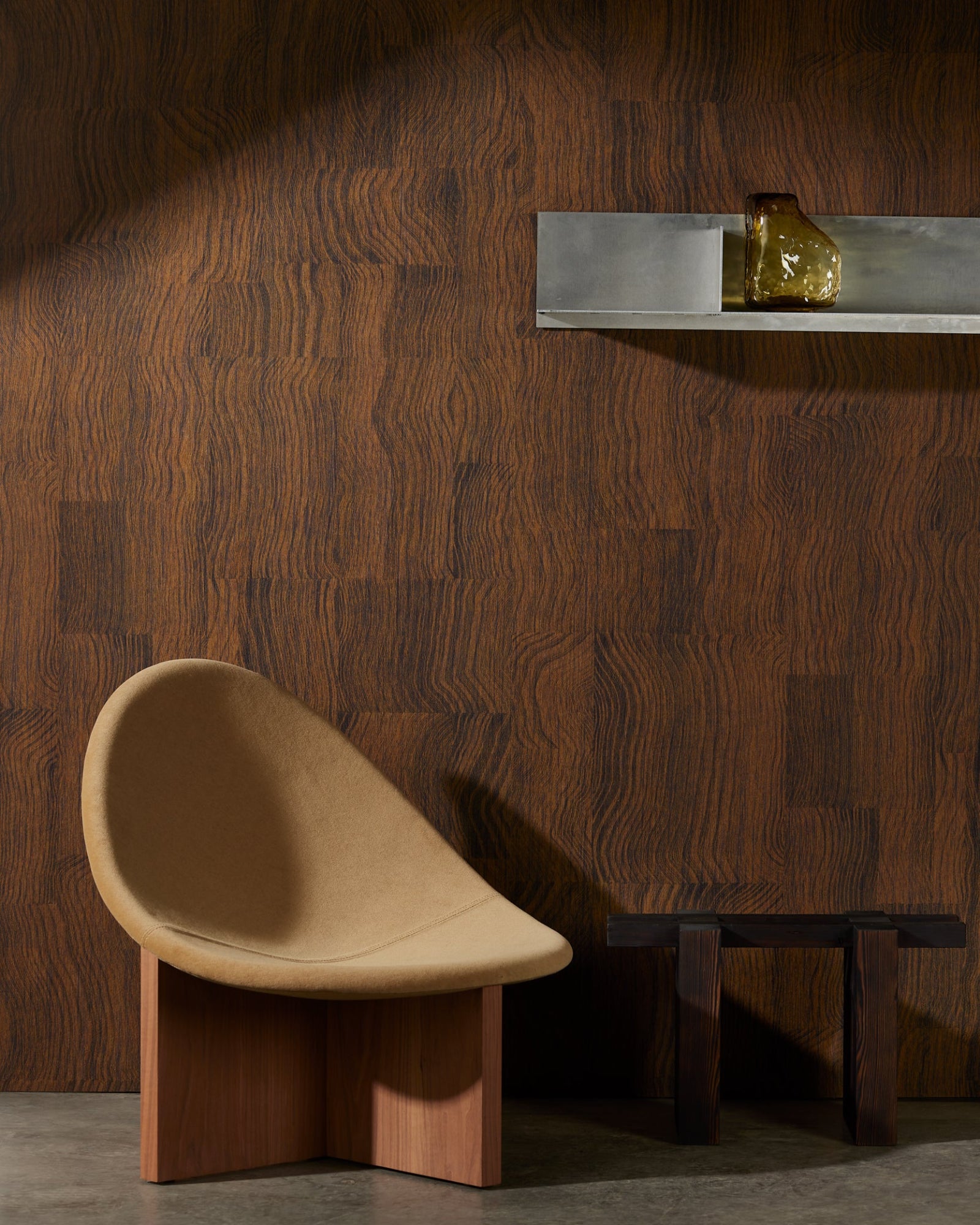 Modern beige accent chair with wooden base beside a small dark wood table, set against a luxury dark wood wall panel in a contemporary interior.