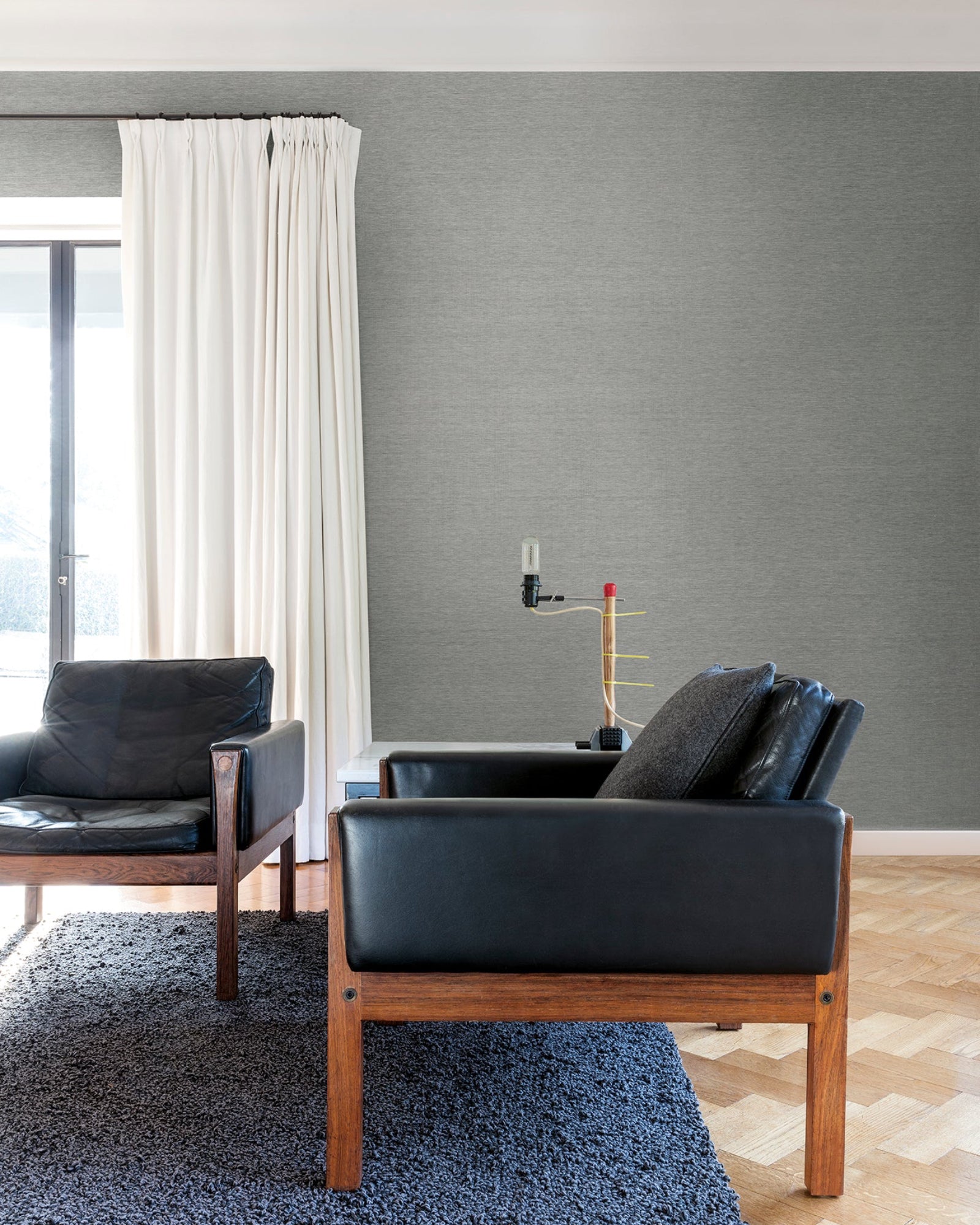Modern living room with black leather armchairs, wooden frames, and a textured grey wall.