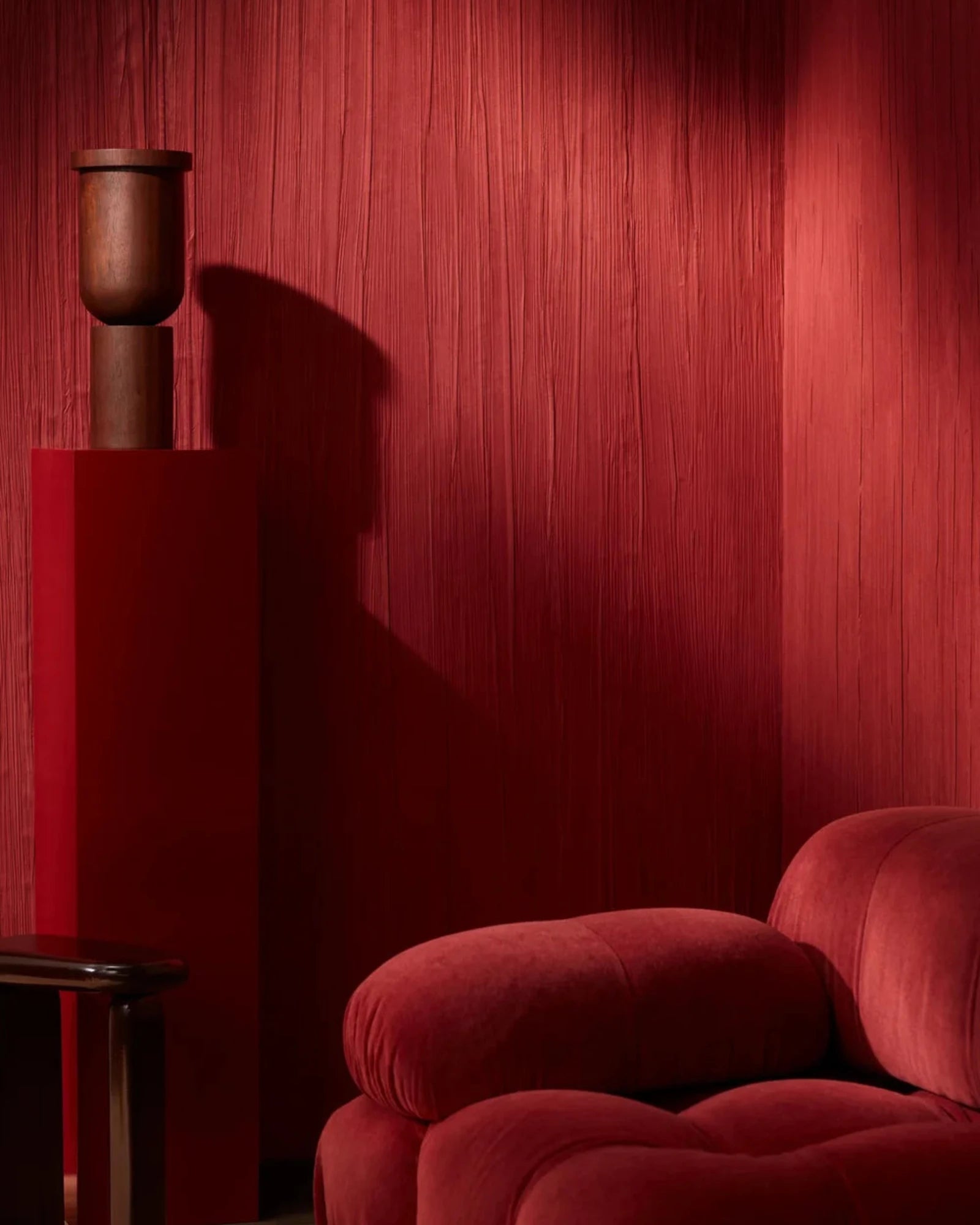 Modern luxury interior with red textured wall, sculptural vase, and plush red armchair