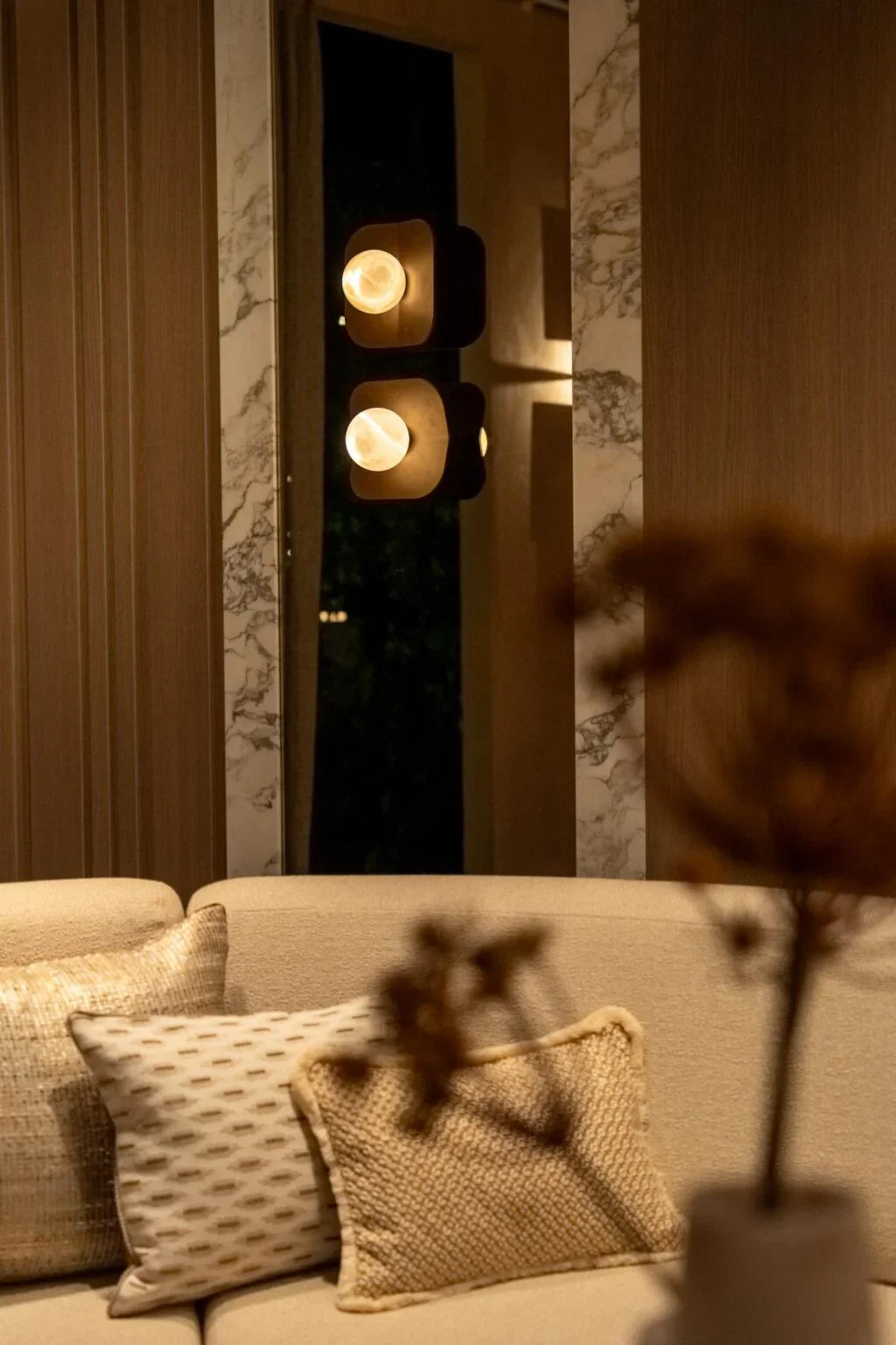 Luxury living room with beige sofa, textured pillows, marble wall accents, and modern wall lights