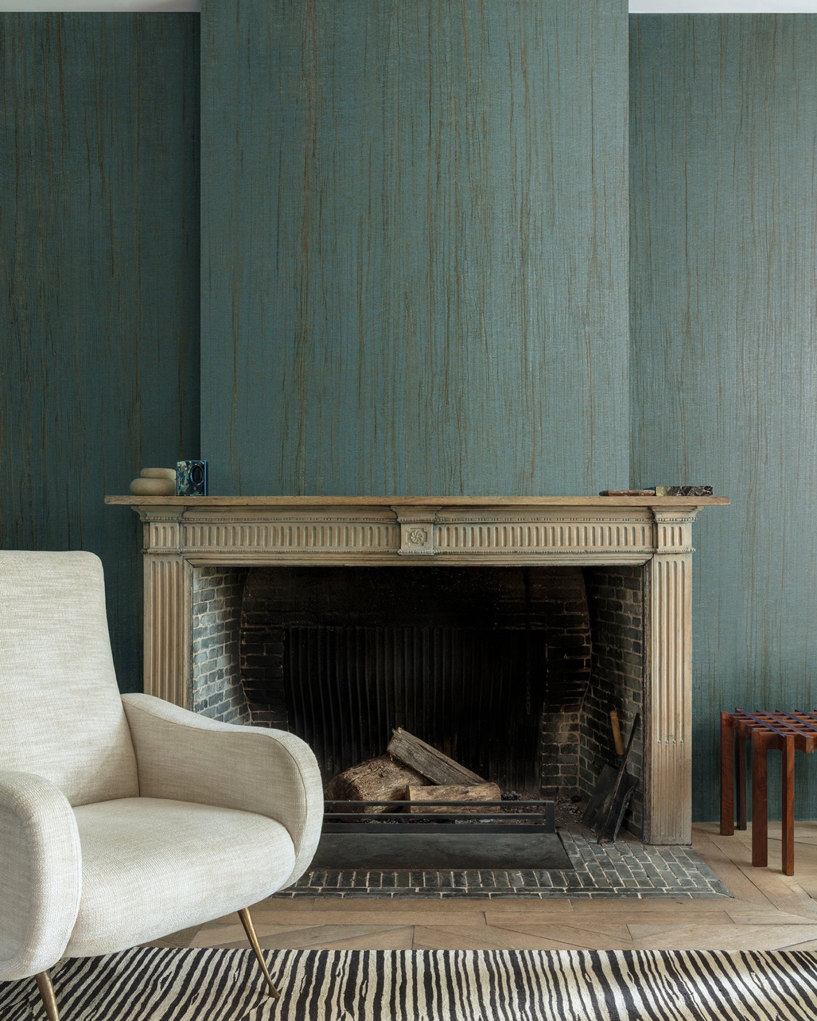 Modern living room with a beige armchair, elegant fireplace, blue textured wall, and wood accents