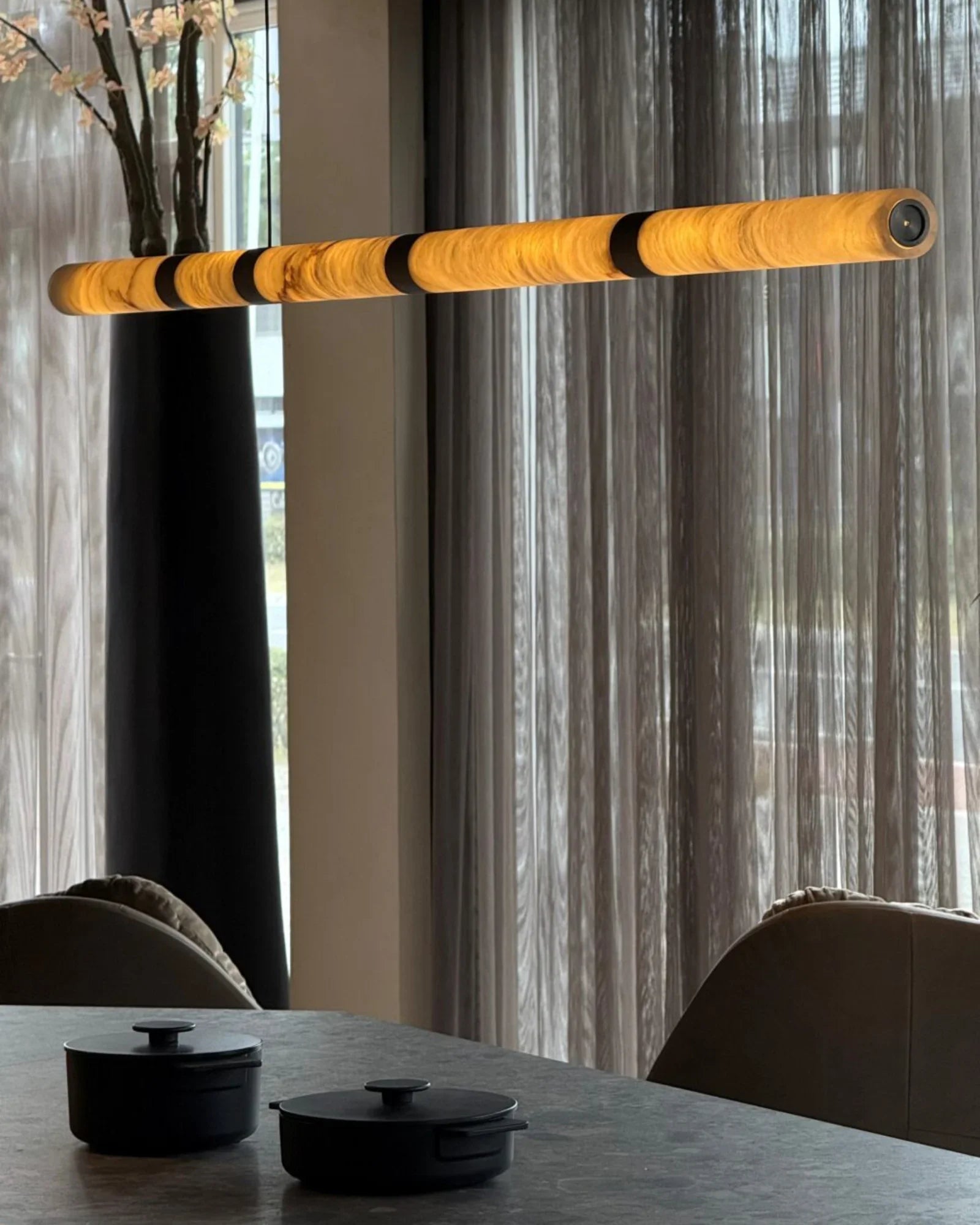 Modern linear pendant light glowing above a dining table with black cookware