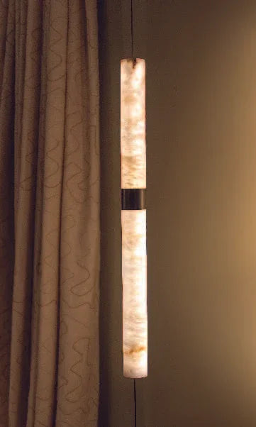 Vertical modern wall light fixture with soft glow beside textured curtain in a luxury interior.