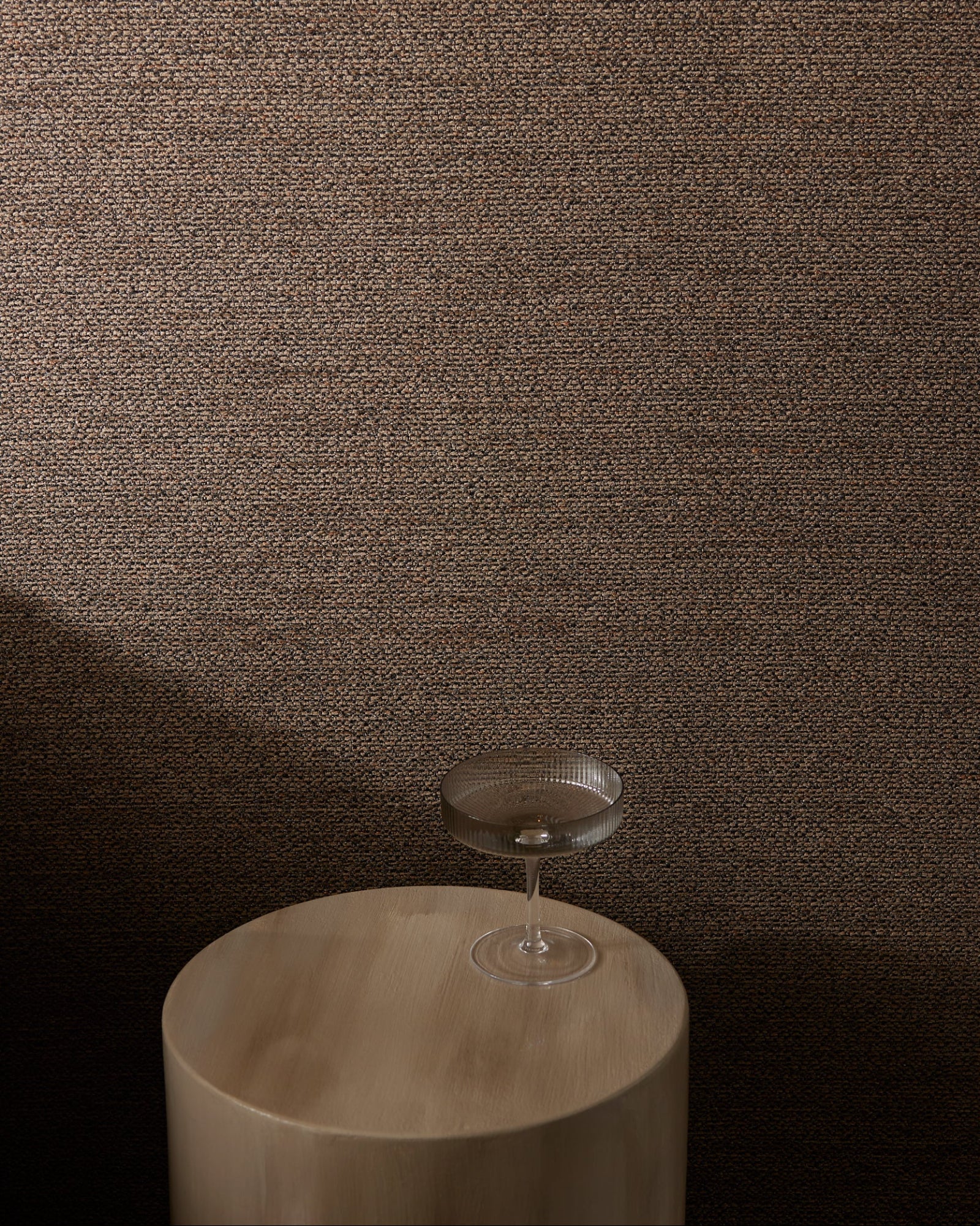 Textured brown wall with a clear glass on a round wooden table, modern interior design