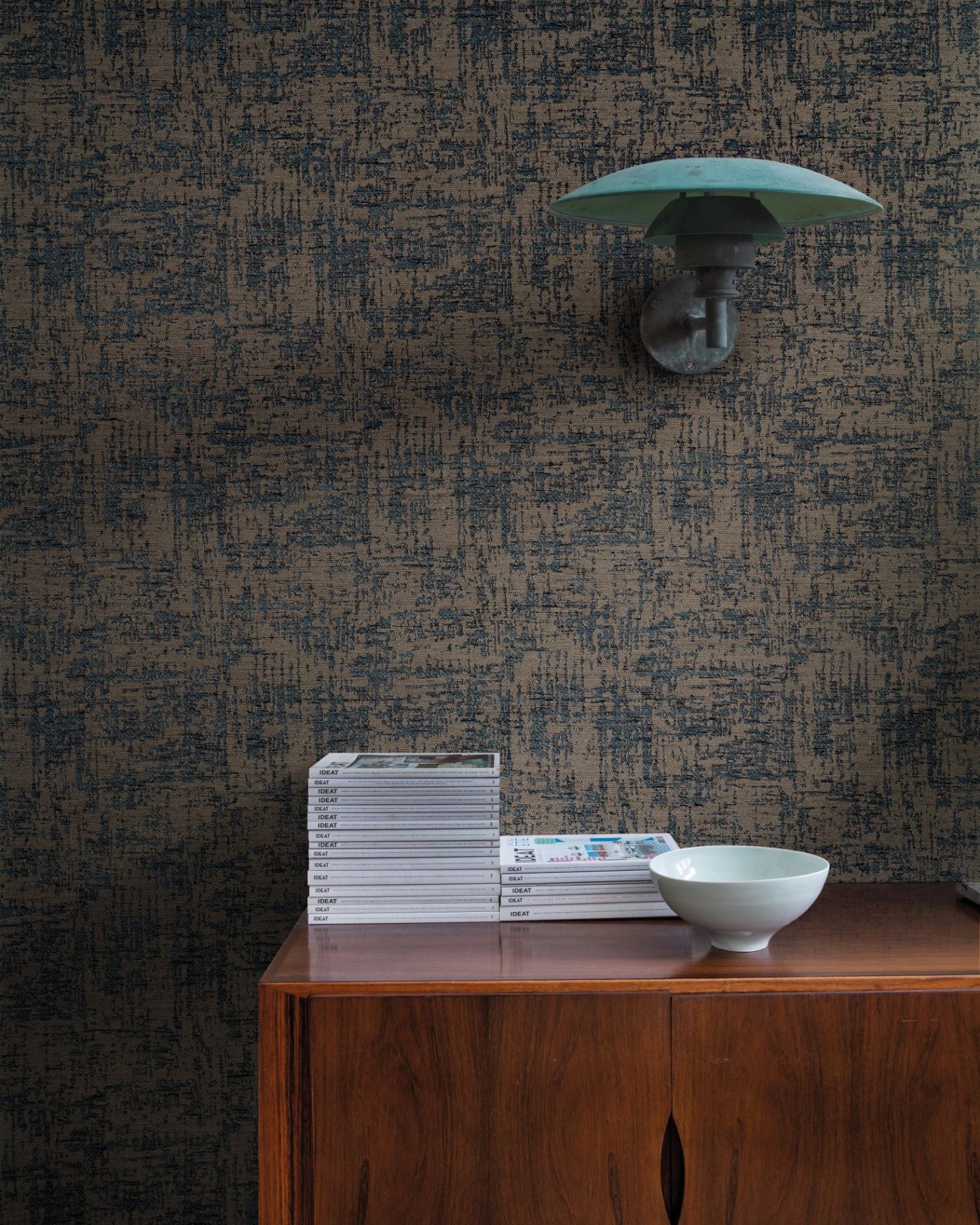 Textured blue and brown patterned wall, modern sconce, wooden console with stacked magazines and a ceramic bowl