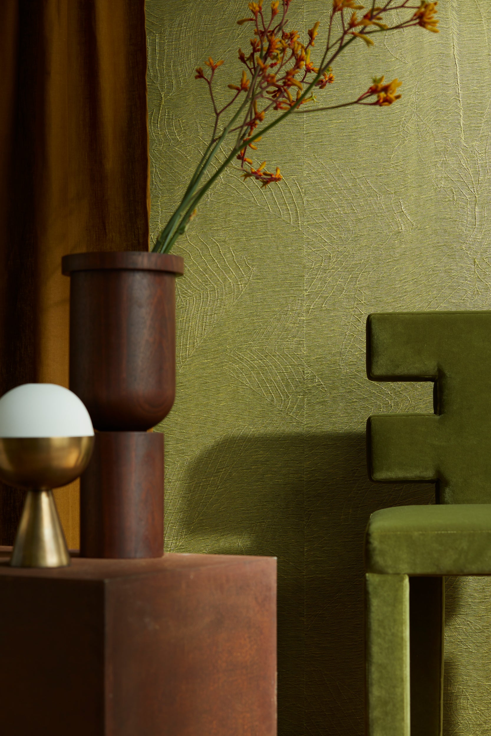 Modern luxury interior with green textured wall, velvet chair, wooden vase and designer lamp