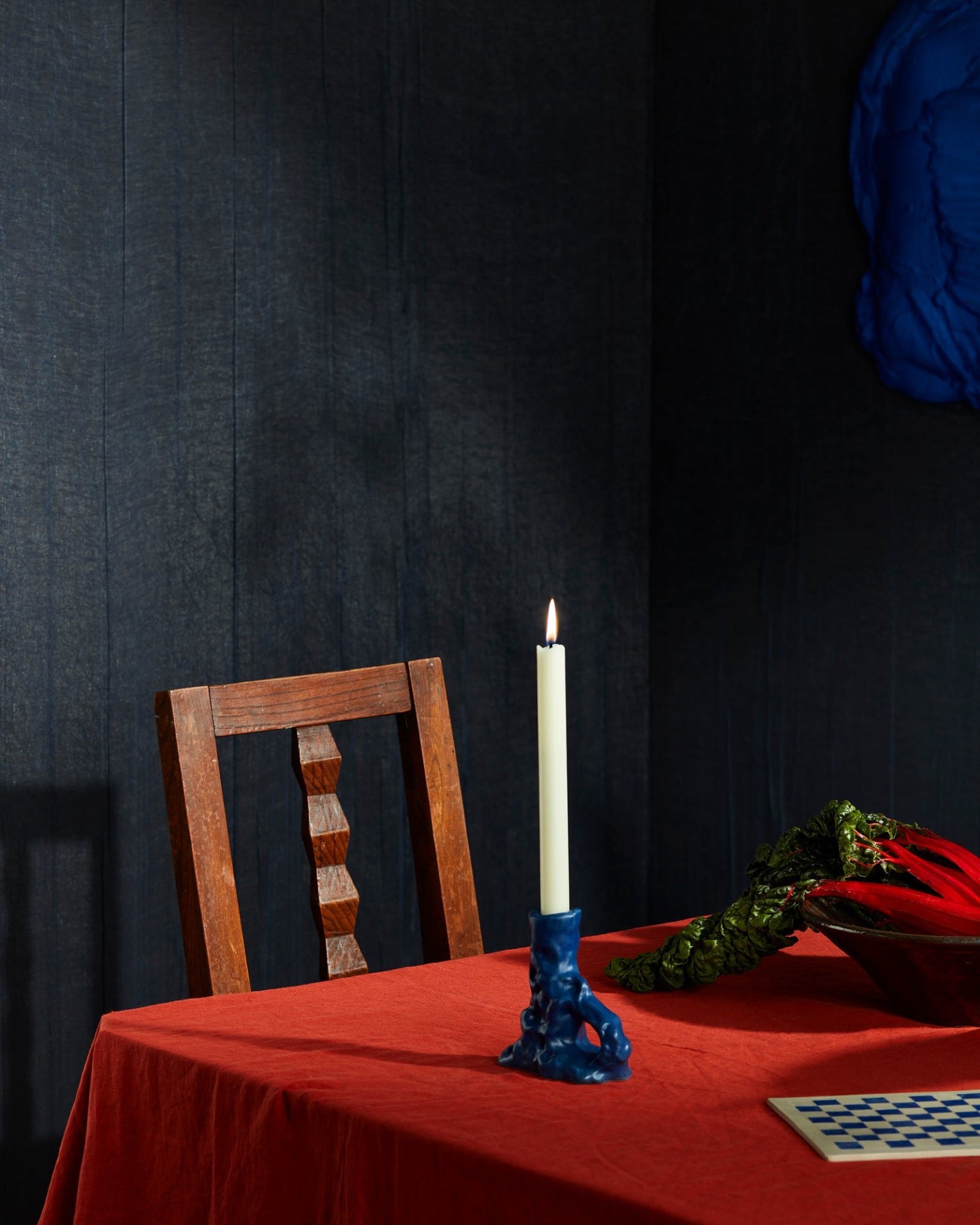 Elegant dining table with red tablecloth, wooden chair, blue candle holder, and leafy centerpiece.