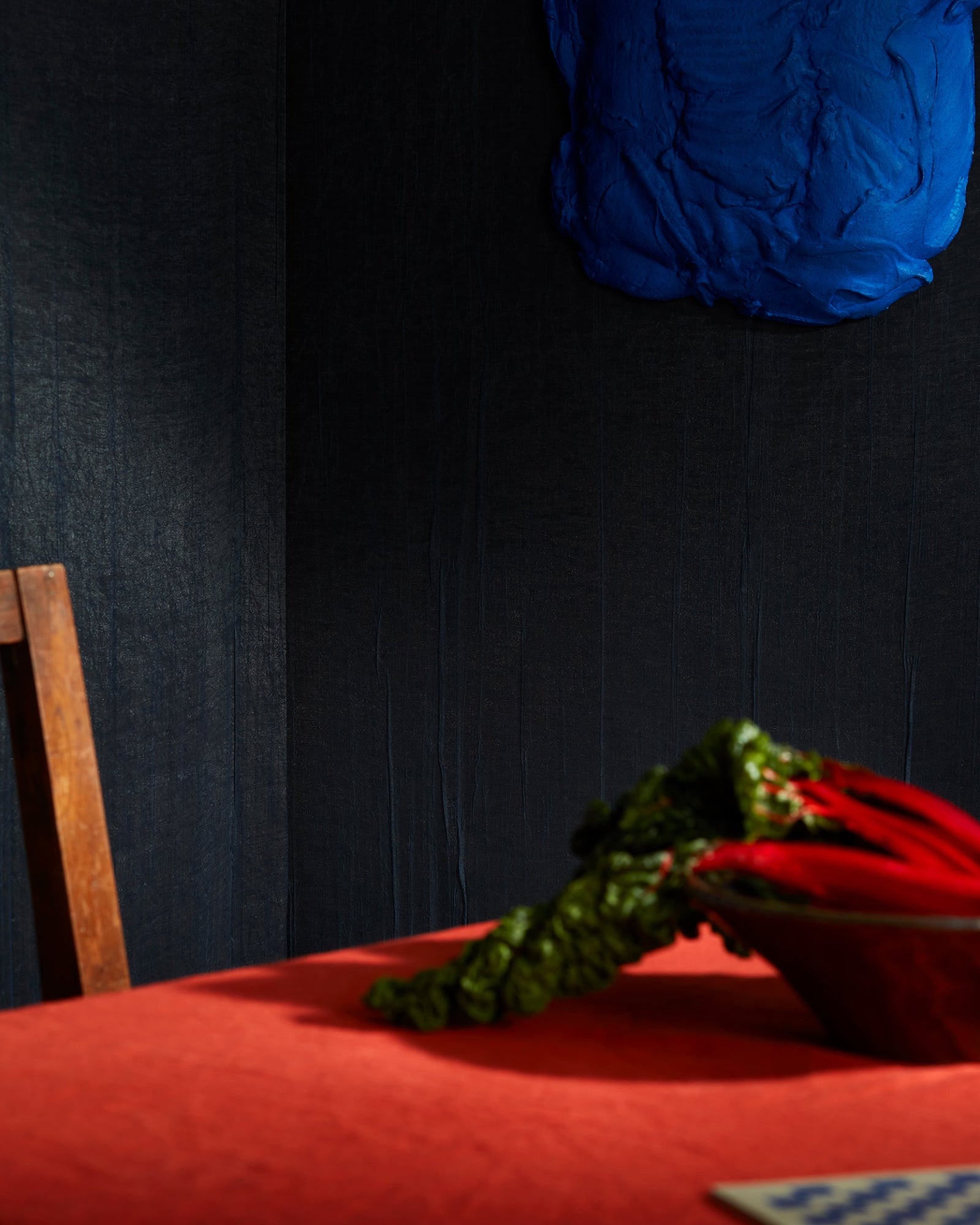 Minimalist luxury dining area with a red tablecloth, wooden chair, and abstract blue wall art