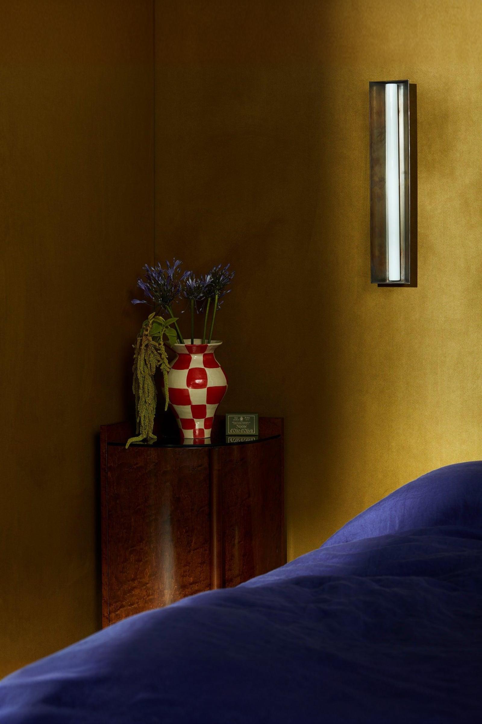 Luxury interior corner with checkered vase, purple flowers, and wall sconce lighting