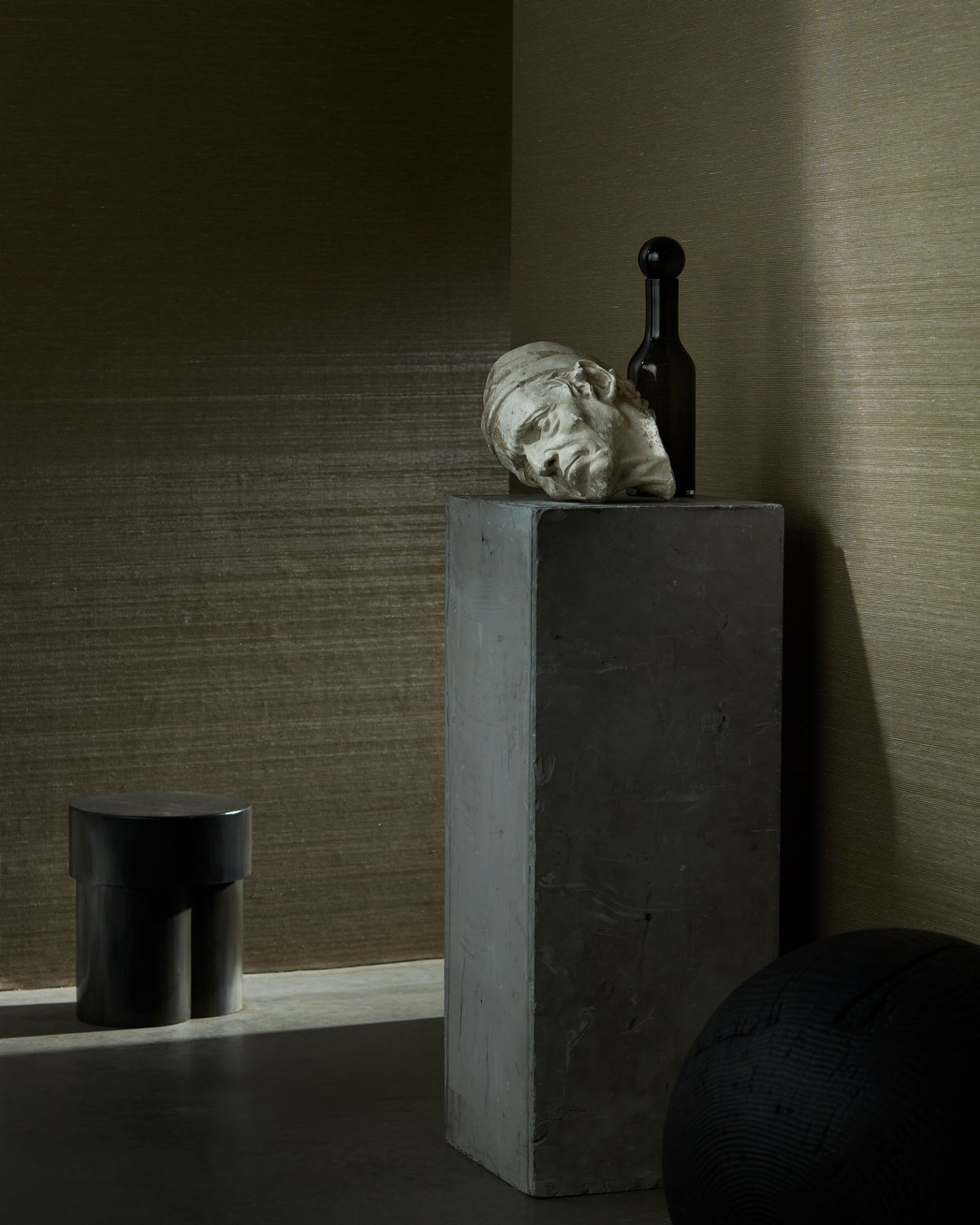 Minimalist luxury interior with concrete pedestal, classical head sculpture, dark bottle and modern stool