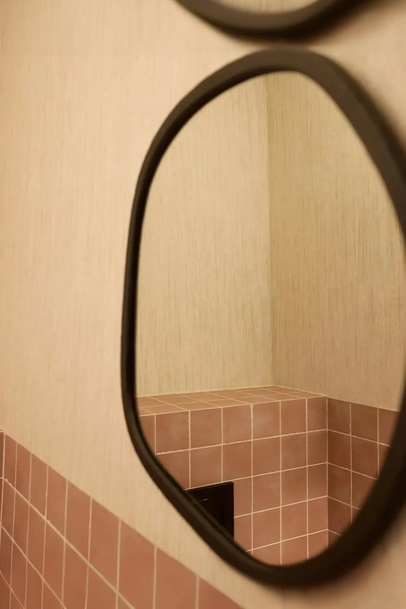 Rounded mirror reflecting beige wall and pink square ceramic tiles in a modern interior