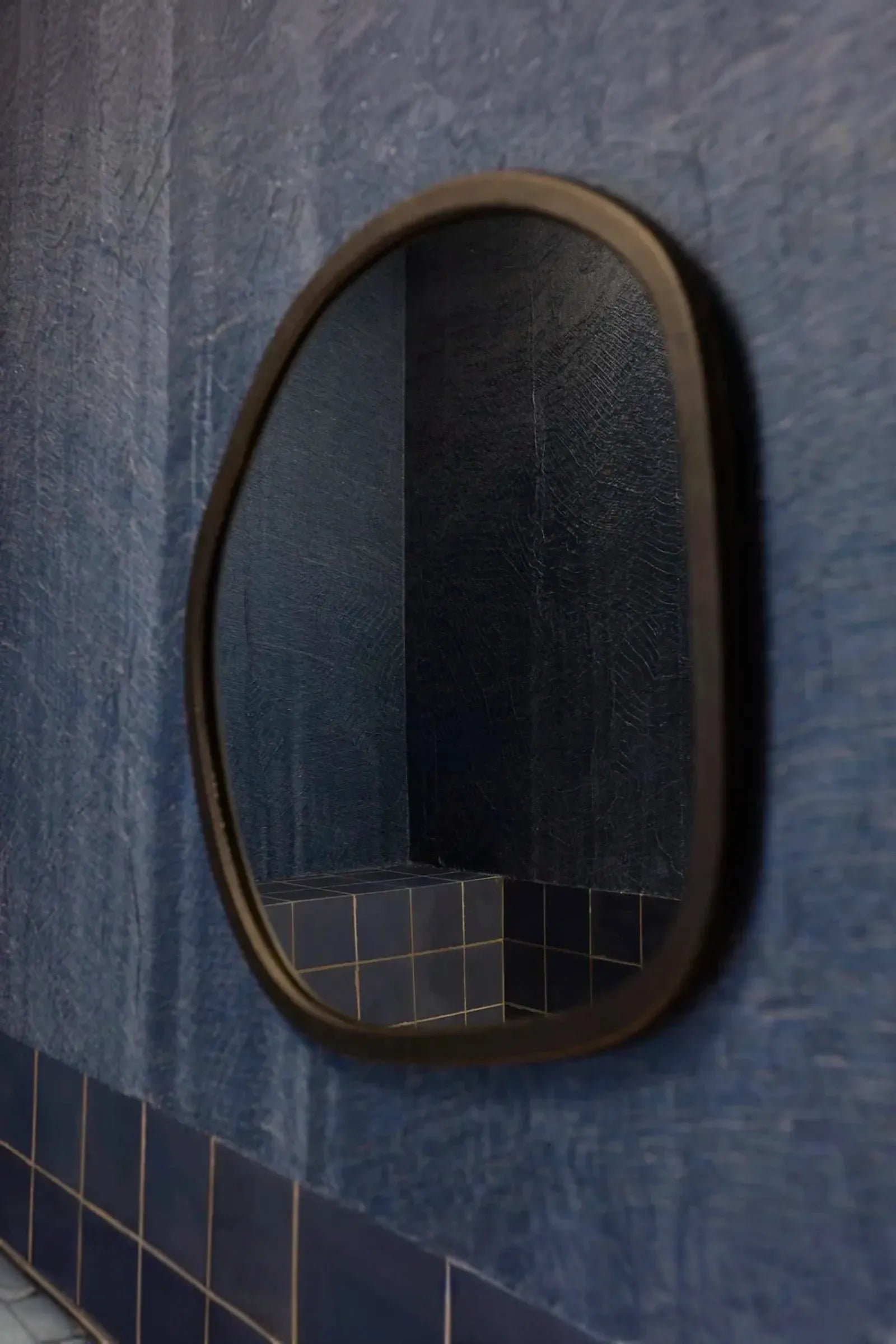 Oval mirror on blue textured wall with matching blue tiled surface, modern luxury interior