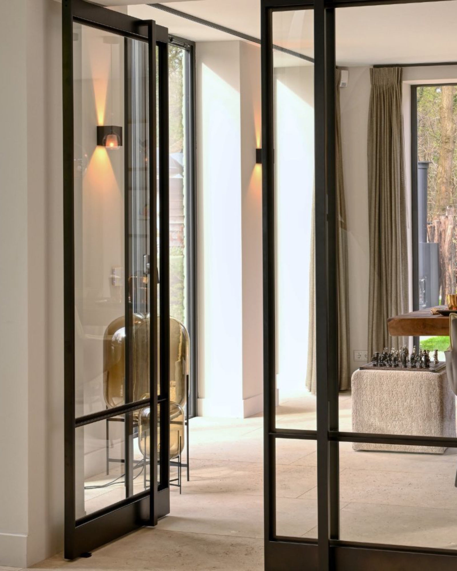 Modern luxury interior with glass and black metal doors, natural light, and elegant furnishings