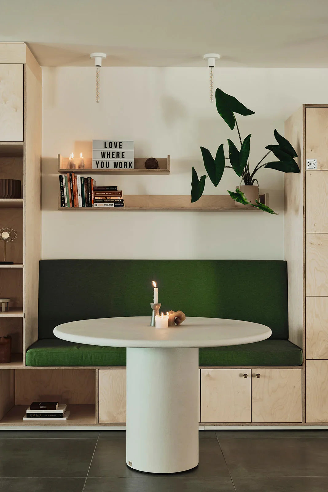 Modern luxury home interior with round table, green bench, candles, books, and large plant