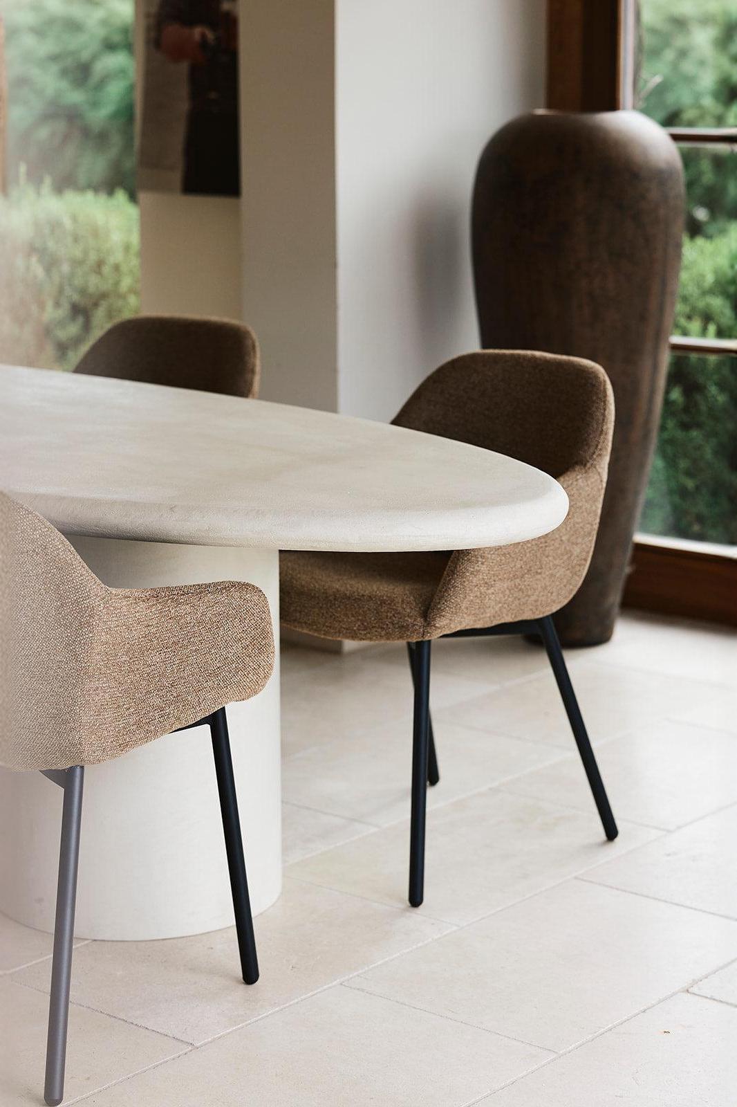 Modern dining area with a round light stone table and brown upholstered chairs in a bright interior