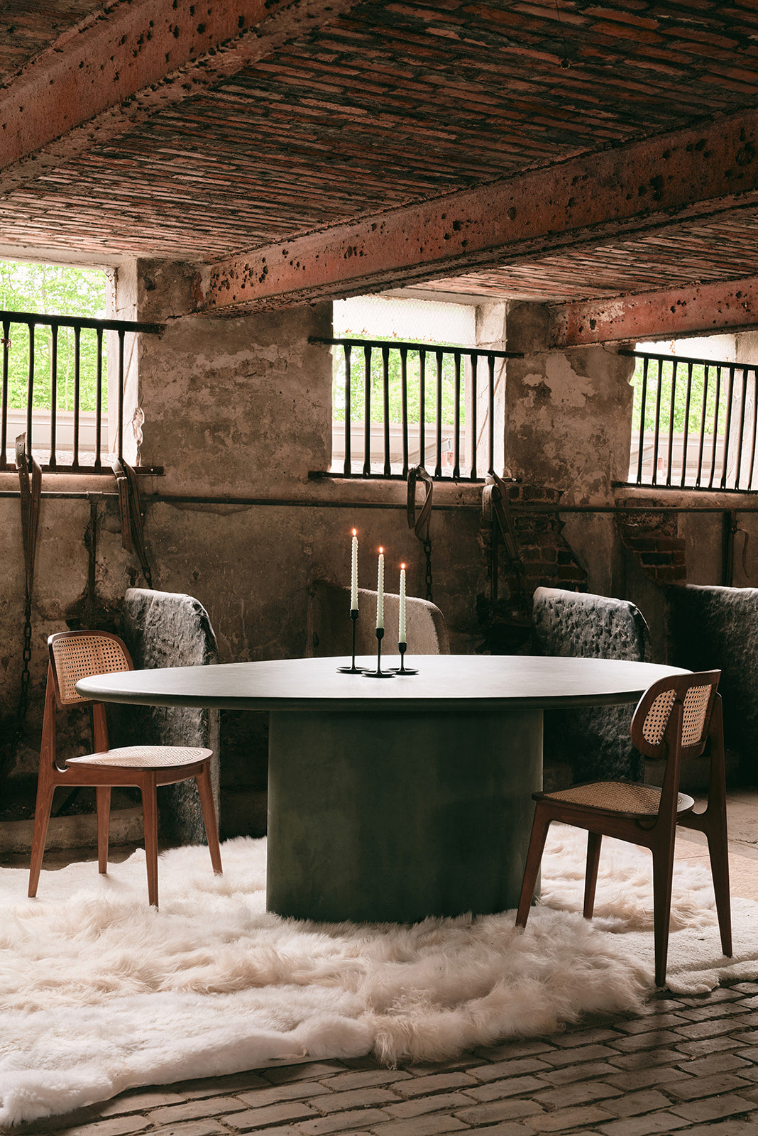 Luxury dining table with candles, wooden chairs, and sheepskin rug in rustic interior setting