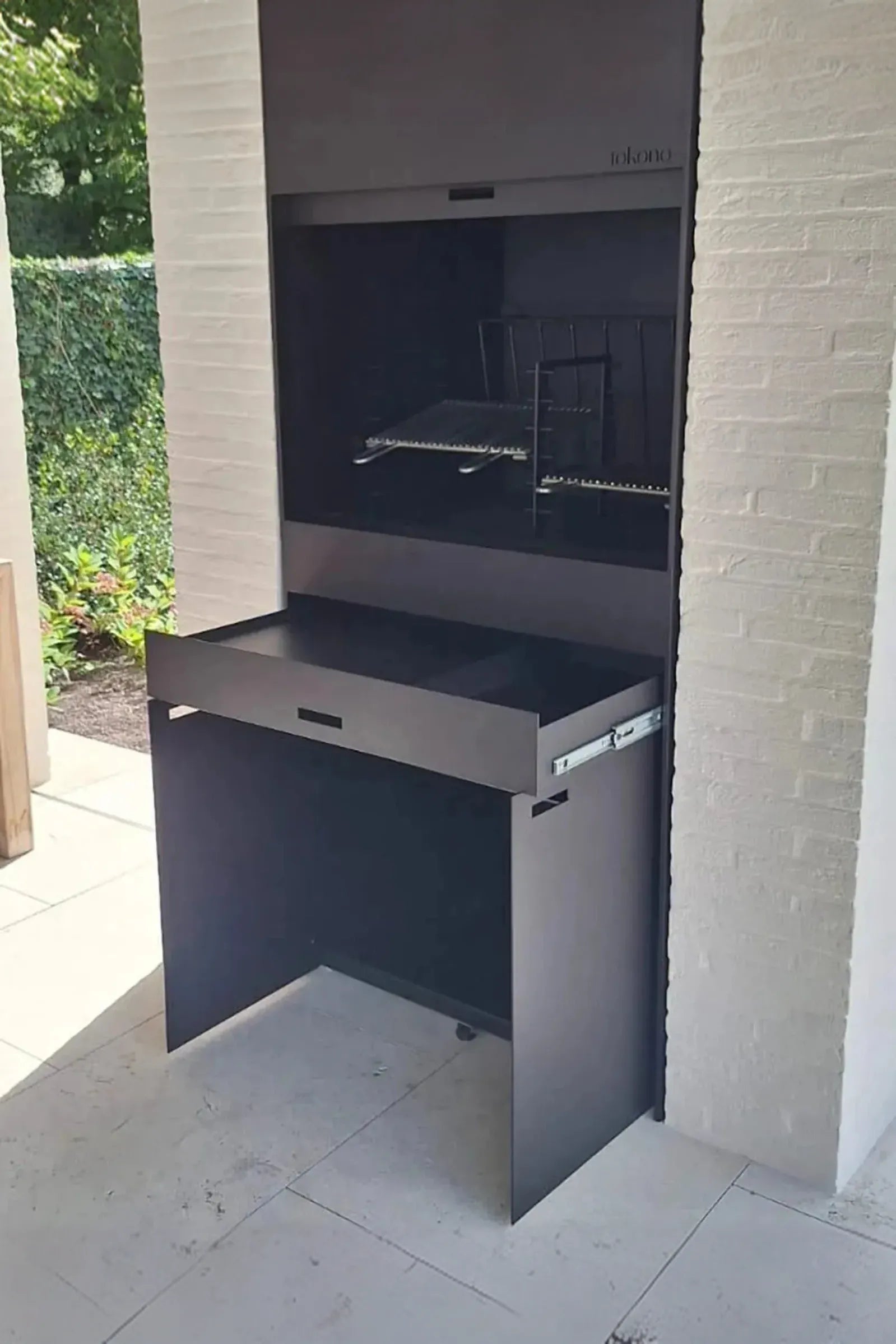 Modern outdoor built-in black metal fireplace and grill against white brick wall